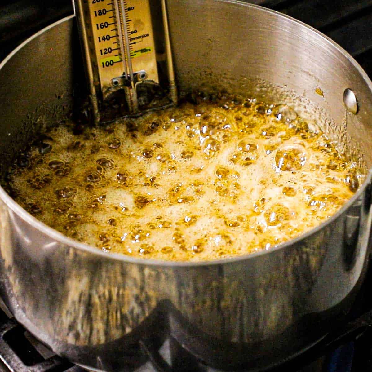 A silver saucepan that is filled with a vigorously bubbling sugar and honey mixture that has turned a deep amber color.