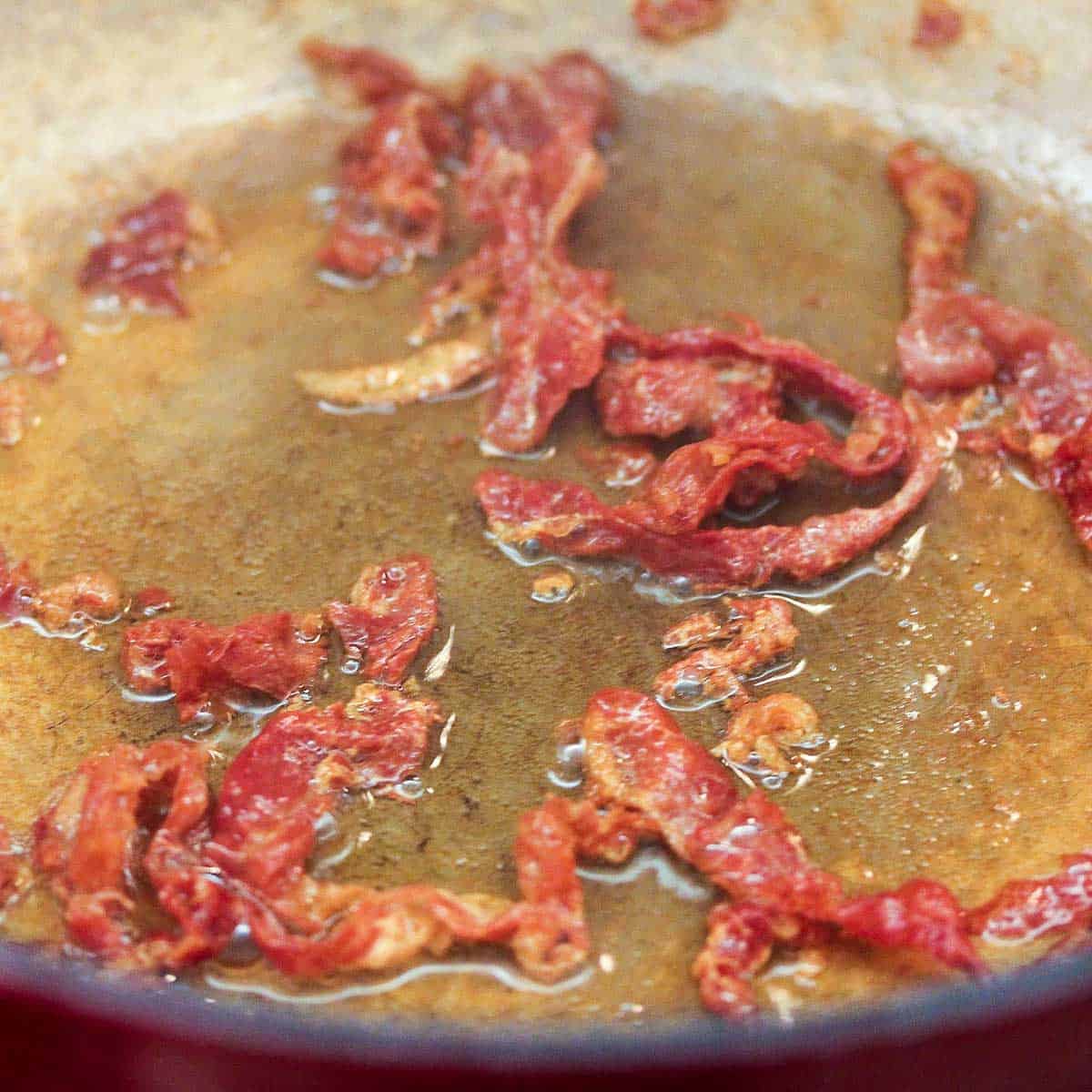 A close-up view of crispy strips of prosciutto being cooked in a skillet and hot oil.
