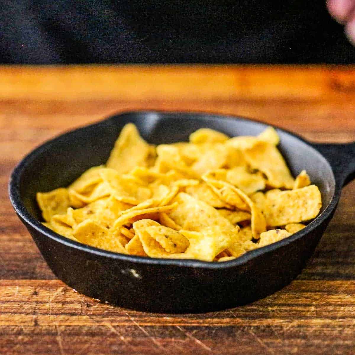 A straight-on view of a small black cast-iron skillet filled with a layer of corn chips.