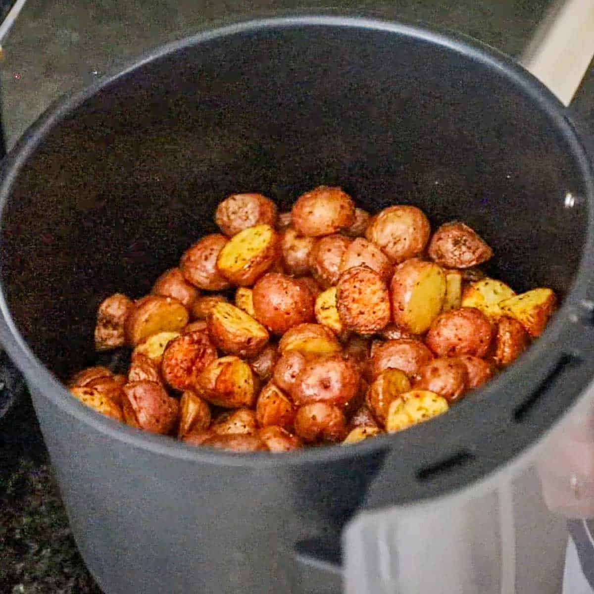 A view into the basket of an air-fryer that is half filled with partially cooked crispy red baby potatoes that have been halved and seasoned and coated in olive oil.
